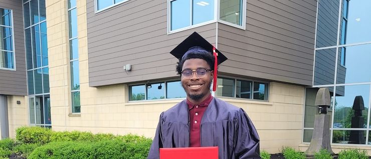 David Watson Jr. dressed in a cap and gown outside the Health Sciences Center on the Blue Bell Campus