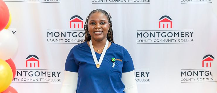 Anthonesha Anguin wears blue scrubs and stands in front of a backdrop that says Montgomery County Community College.