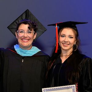 Caitlin Campbell and Michelle Kulla are smiling on stage with Caitlin holding an associate's degree.
