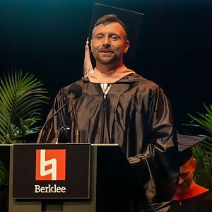 Colin Foley dressed in a black cap and gown delivers a speech at a lectern. 