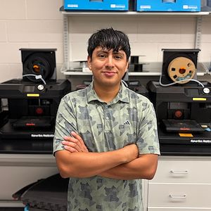 Heber Herrera stands arms crossed in front of engineering equipment. 