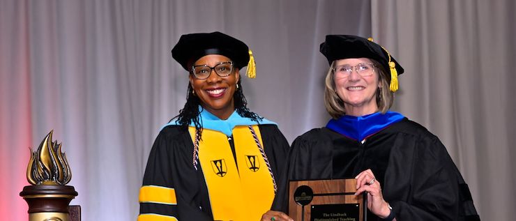 Dr. Sweet and Dr. Bryans hold Lindback plaque. Dr. Chae Sweet and Dr. Margaret Bryans in academic regalia stand next to each other as Dr. Bryans holds a Linback Distinguished Teaching Award plaque during Commencement