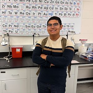 Oscar Amador stands in front of a periodic table of elements in a classroom. 