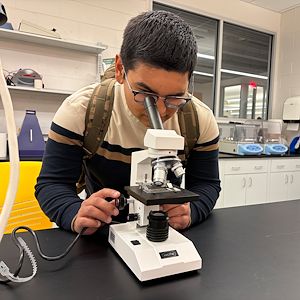 Oscar Amador inspects a slide under a microscope in a science classroom. 