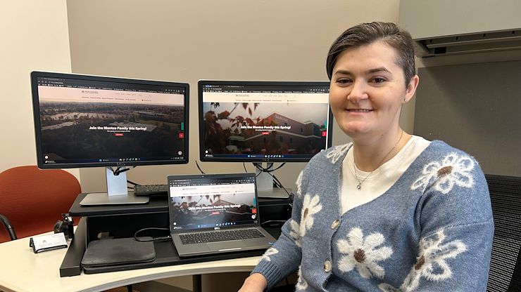 Taylor Bellegue sits at a computer desk smiling. She has two monitors with the Montgomery County Community College home page on the screens behind her. 